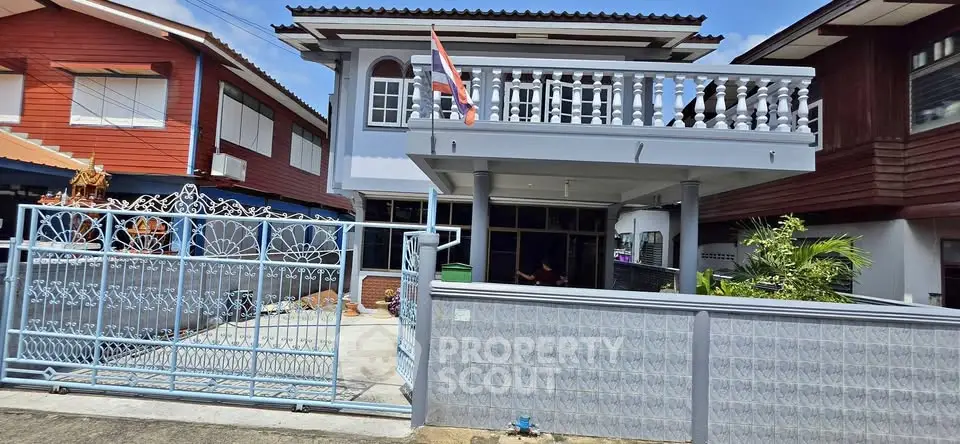 Charming two-story house with balcony and gated entrance in a serene neighborhood.