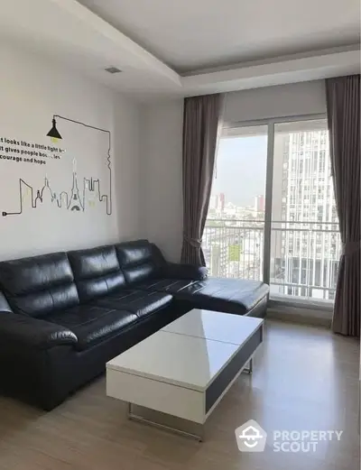 Spacious living room with sleek black leather sofa, modern white coffee table, and large windows offering ample natural light and a city view.