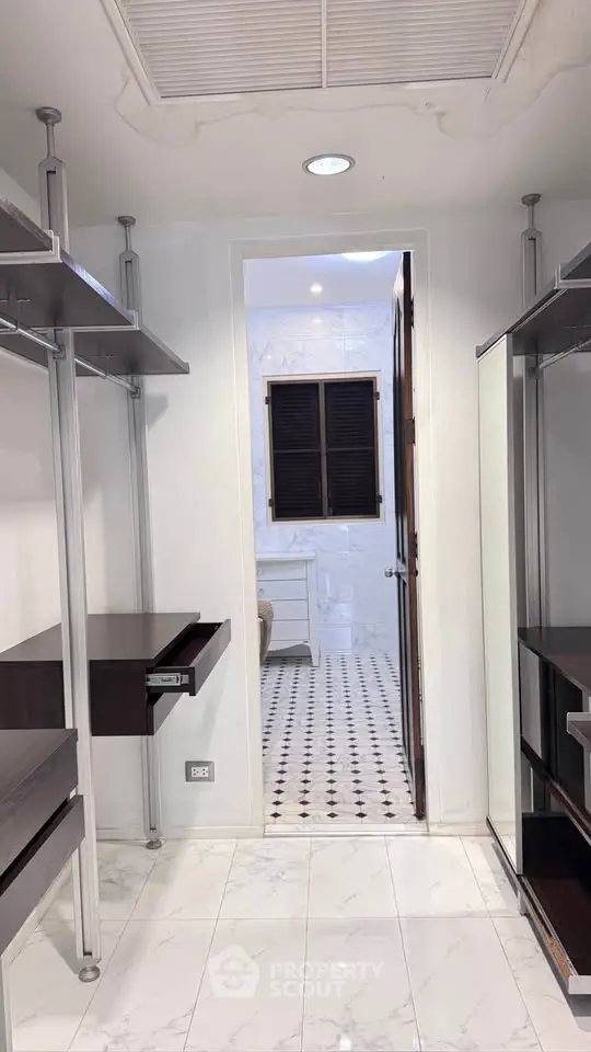 Spacious walk-in closet with modern shelving and view into elegant bathroom.