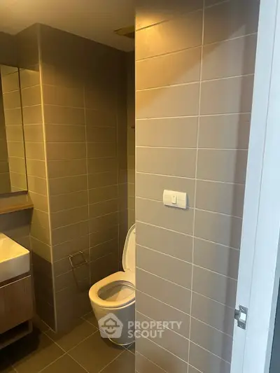 Modern bathroom with sleek design and neutral tiles, featuring a toilet and stylish sink.
