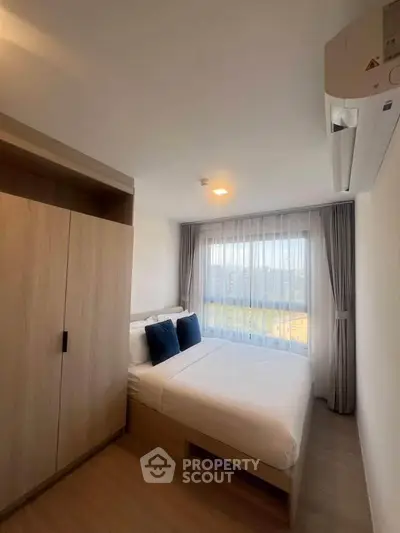 Cozy bedroom with large window and modern air conditioning unit, perfect for relaxation.