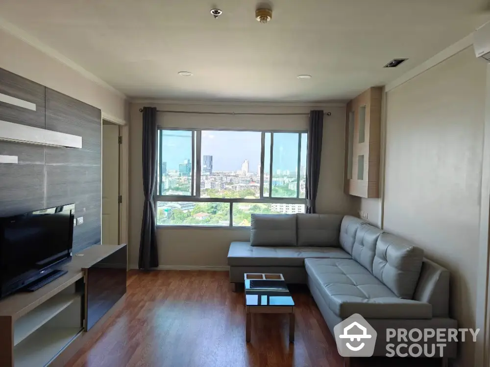 Modern living room with large window and city view, featuring sleek furniture and wooden flooring.