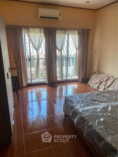 Spacious bedroom with large windows and balcony access, featuring polished wooden floors and modern air conditioning.