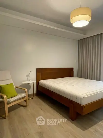 Modern bedroom with wooden bed frame, cozy chair, and soft lighting