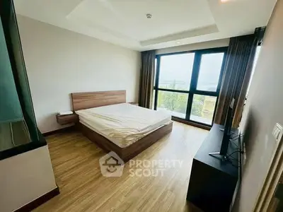 Spacious bedroom with large window offering stunning views, featuring modern furnishings and wooden flooring.
