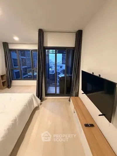 Modern bedroom with large windows and wall-mounted TV, offering a city view from the balcony.