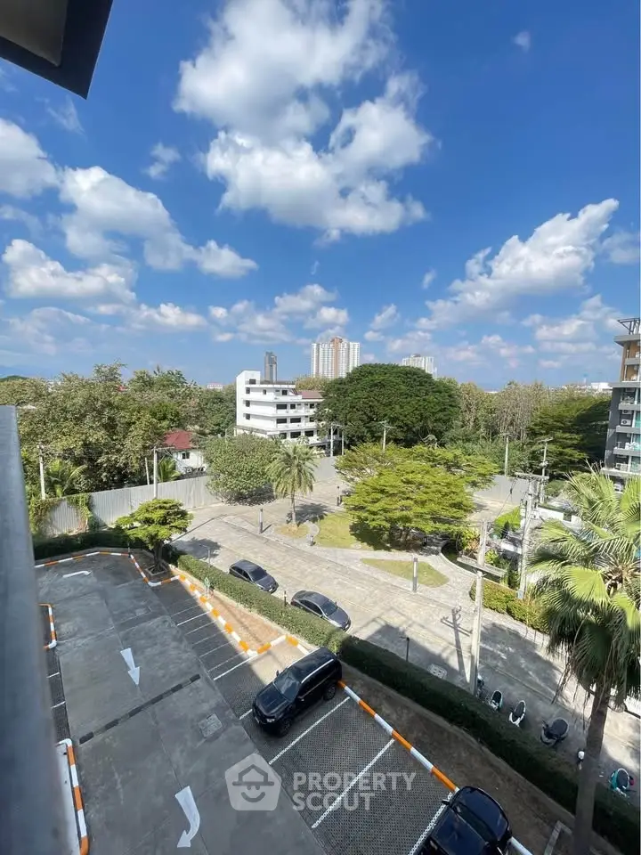 Scenic view from balcony overlooking parking area and lush greenery under a clear blue sky.