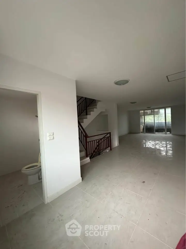 Spacious open-plan living area with staircase and large windows for natural light.
