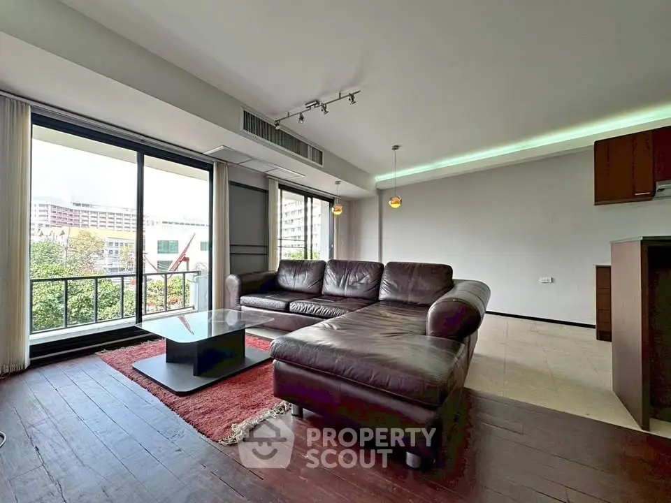 Spacious living room with modern leather sofa and city view balcony.