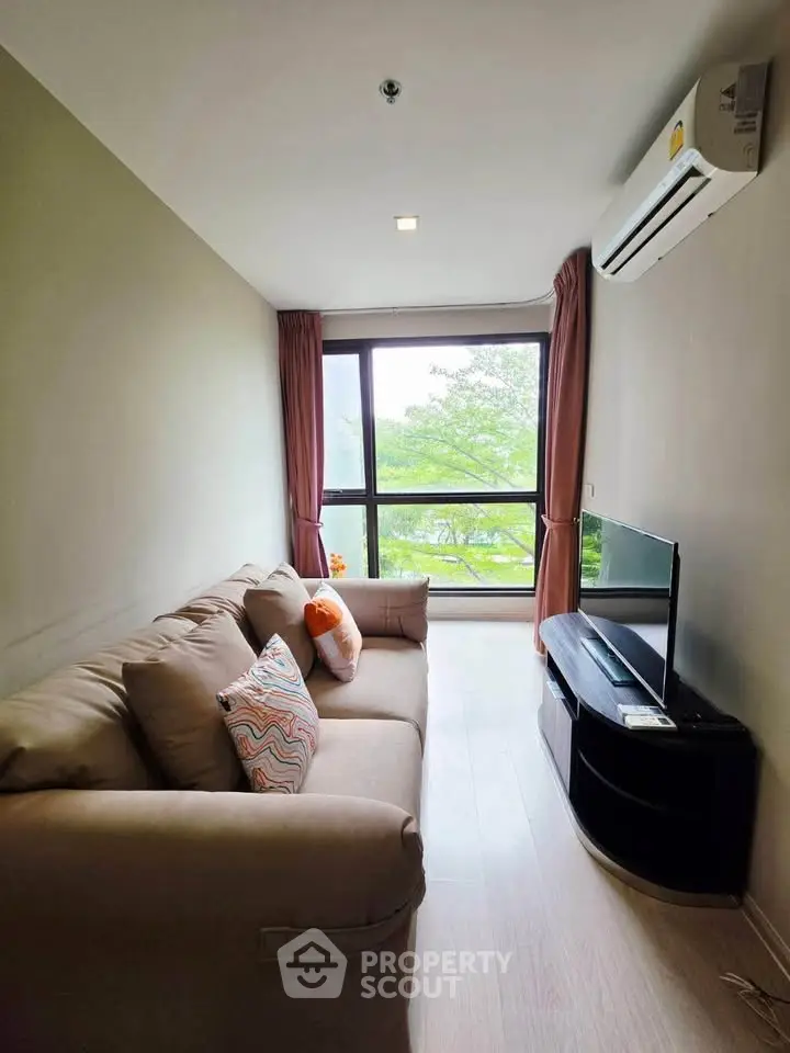 Cozy living room with large window and modern furnishings, offering a serene view of greenery.