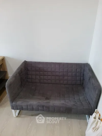 Modern gray sofa in a minimalist living room setting with light wood flooring.