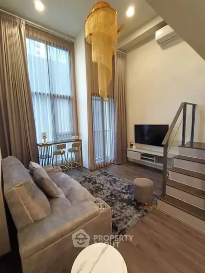 Modern living room with high ceilings, elegant chandelier, and cozy seating area in a stylish apartment.