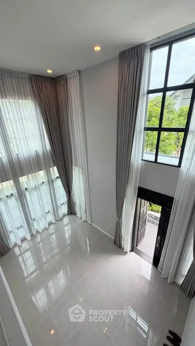 Spacious modern living room with high ceilings and large windows, offering abundant natural light and elegant curtains.