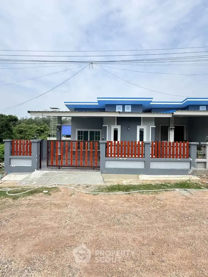 Modern single-story house with blue roof and wooden gate, showcasing a spacious front yard.