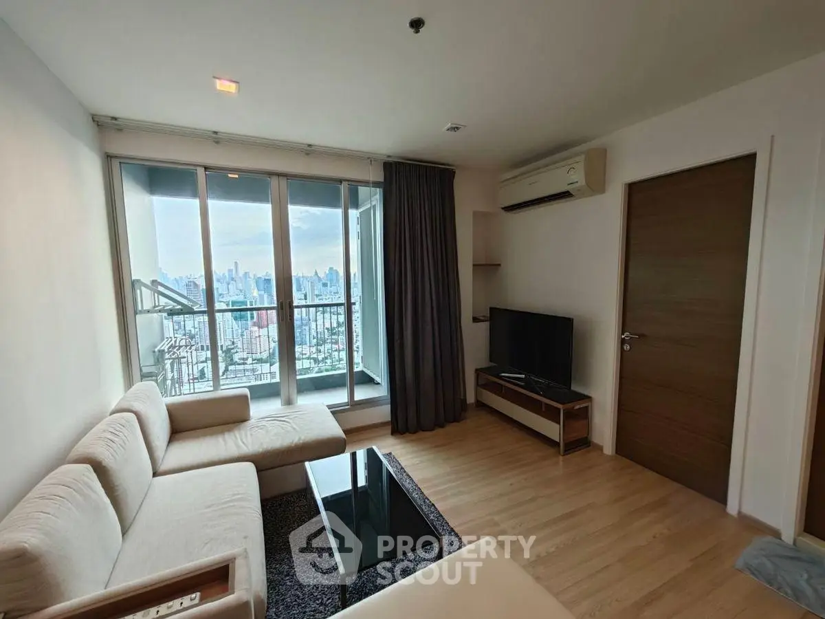 Modern living room with city view, featuring sleek furniture and large windows.