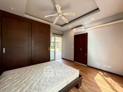 Spacious bedroom with wooden flooring and ceiling fan, featuring large windows for natural light.