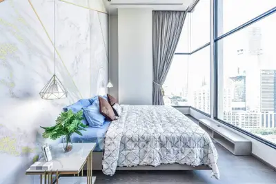 Luxurious bedroom with floor-to-ceiling windows offering stunning city views, modern decor, and elegant lighting.