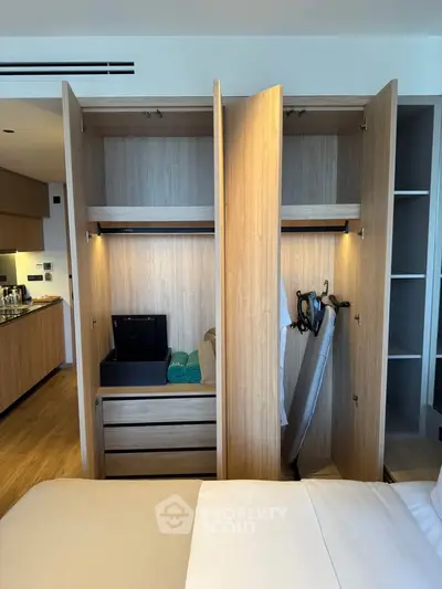 Modern bedroom with open wardrobe showcasing ironing board and storage space.