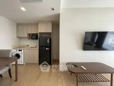 Modern apartment interior with compact kitchen and cozy living area, featuring a washing machine and flat-screen TV.