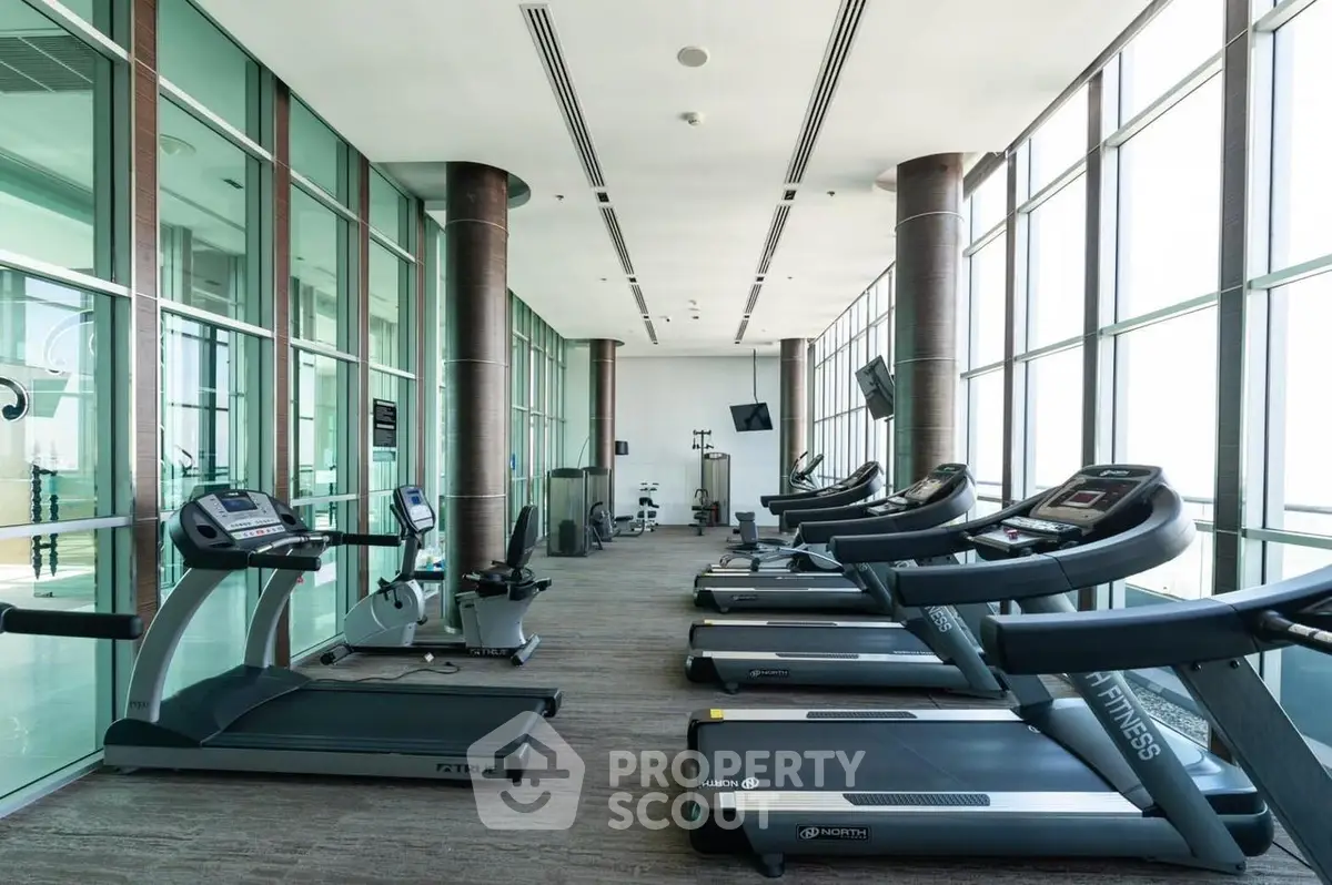 Spacious modern gym with large windows and multiple treadmills in luxury residential building.