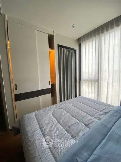Modern bedroom with large window and built-in closet, featuring cozy bedding and natural light.
