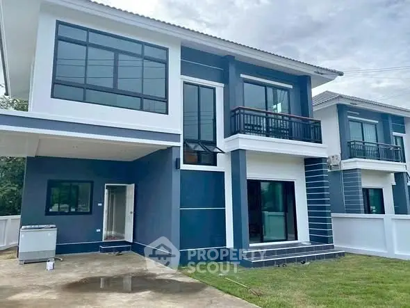Modern two-story blue house with large windows and a spacious driveway.