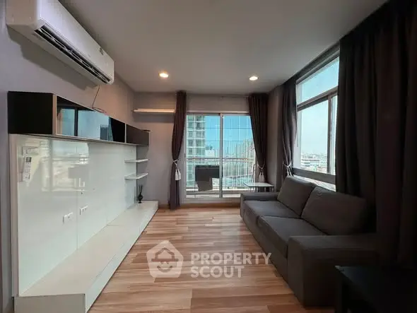 Modern living room with large windows and city view, featuring sleek furniture and wooden flooring.