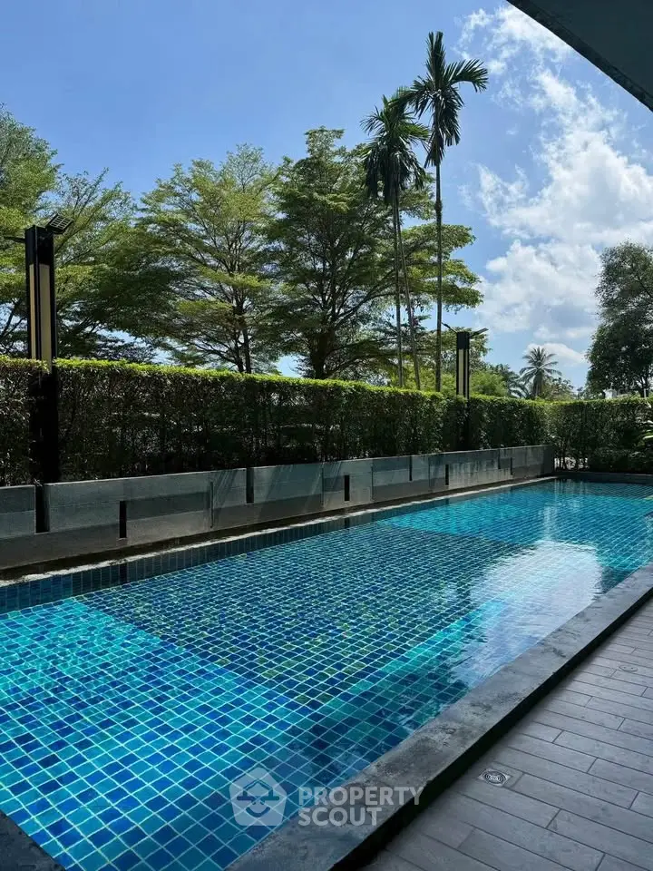 Luxurious outdoor pool with lush greenery and clear blue skies, perfect for relaxation and leisure.