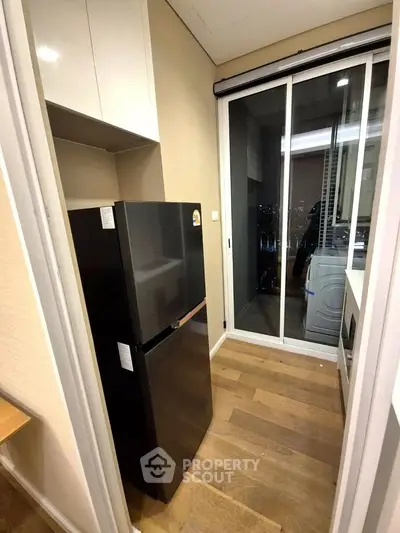 Modern kitchen with sleek black fridge and wooden flooring, featuring a sliding glass door.