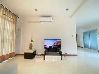 Spacious living room with modern decor and natural light, featuring a TV and air conditioning.