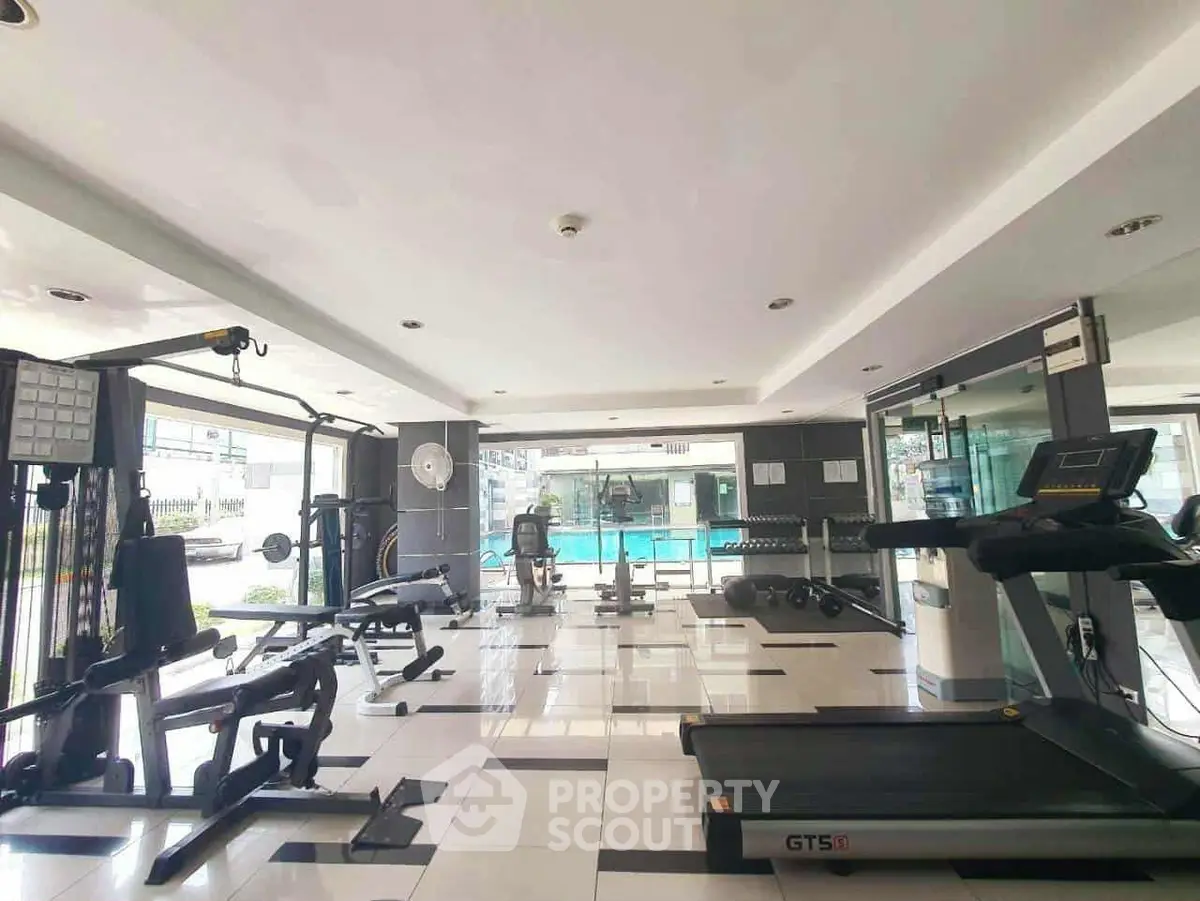 Spacious gym with modern equipment and pool view in luxury apartment complex.