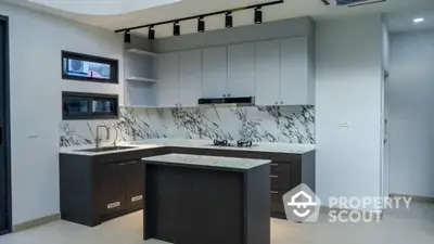 Modern kitchen with marble backsplash and island, featuring sleek cabinetry and gas stove.