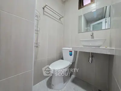 Modern bathroom with sleek fixtures and neutral tiles, featuring a toilet and stylish sink.