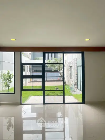 Spacious living room with large windows overlooking a lush garden, offering abundant natural light and serene views.