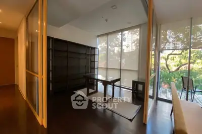 Spacious modern living room with floor-to-ceiling windows and a serene view of lush greenery.