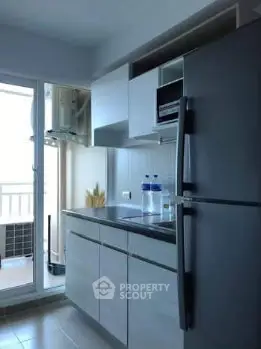 Modern kitchen with sleek cabinets and large fridge, adjacent to a balcony with natural light.