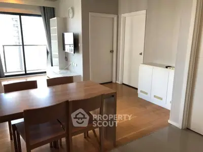 Modern dining area with wooden table and chairs, adjacent to a bright living room with balcony view.