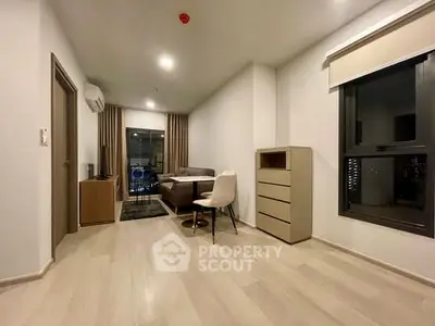 Modern living room with sleek furniture and large window offering city views.