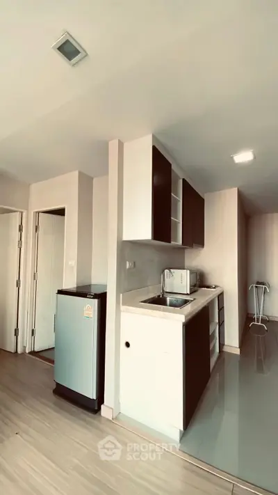 Modern kitchen with sleek cabinetry and compact fridge in open layout apartment.