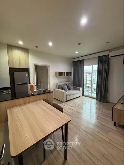 Modern open-plan living room with kitchen, featuring sleek wooden furniture and natural light.