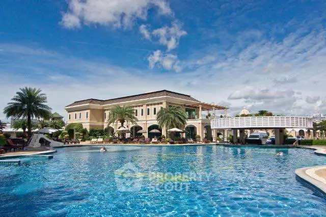 Luxurious resort-style pool with elegant building and palm trees under a clear blue sky.