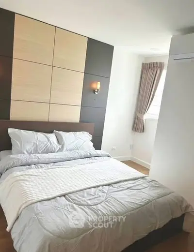 Modern bedroom with stylish decor and natural light, featuring a cozy bed and elegant wall paneling.