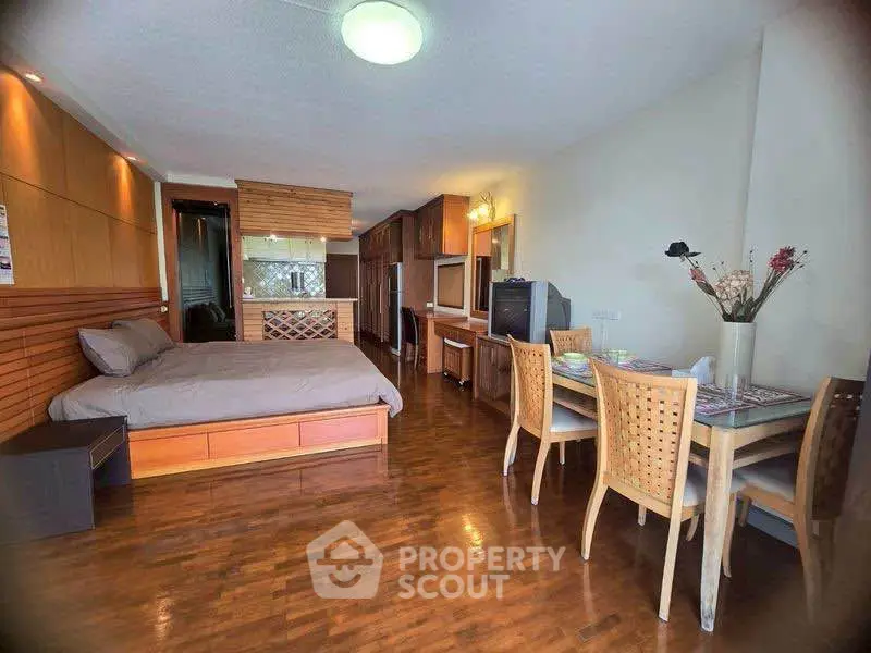 Spacious studio apartment with wooden flooring and modern furnishings, featuring a cozy dining area and comfortable bed.