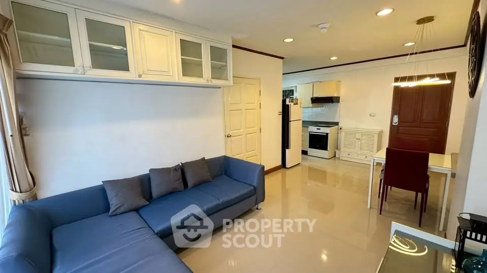 Spacious living room with modern kitchen in open layout, featuring sleek blue sofa and dining area.