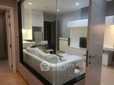 Modern living room with glass partition, sleek white furniture, and integrated kitchen area.