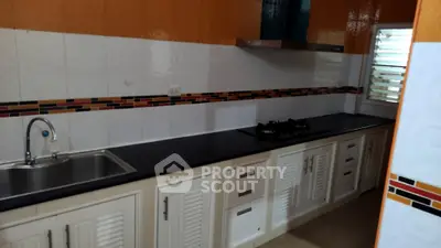Modern kitchen with sleek black countertop and gas stove, featuring vibrant orange and white tile backsplash.