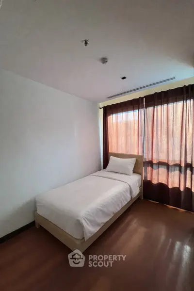 Cozy bedroom with natural light and minimalist design, featuring a single bed and large window with curtains.