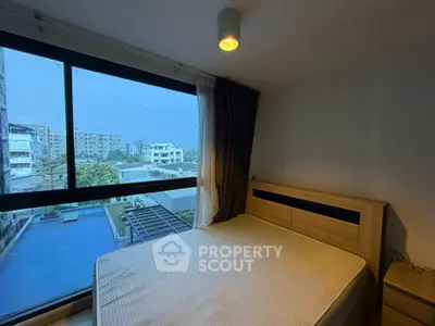 Modern bedroom with large window overlooking pool and cityscape, featuring cozy wooden bed frame.