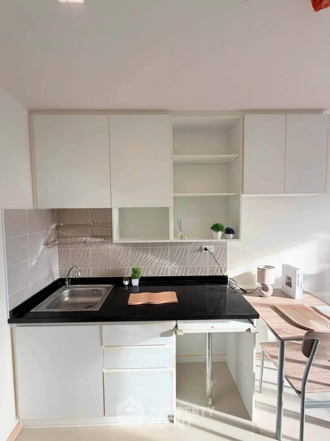Modern kitchen with sleek black countertop and white cabinets, featuring a cozy dining area.