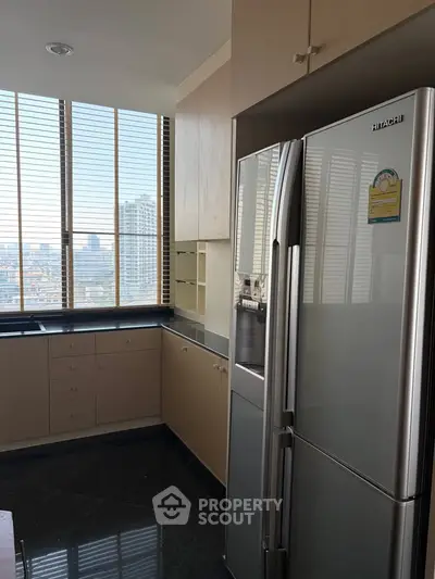 Modern kitchen with sleek refrigerator and city view from large windows.